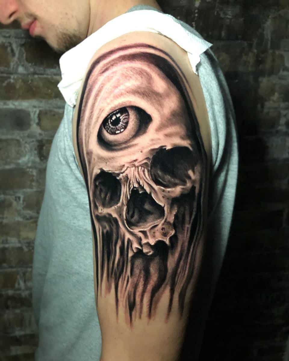 Man's arm with a 3D skull tattoo featuring an eye on the shoulder