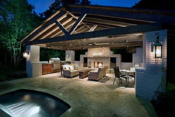 Luxurious outdoor pavilion with fireplace, seating area, dining table, and built-in kitchen.