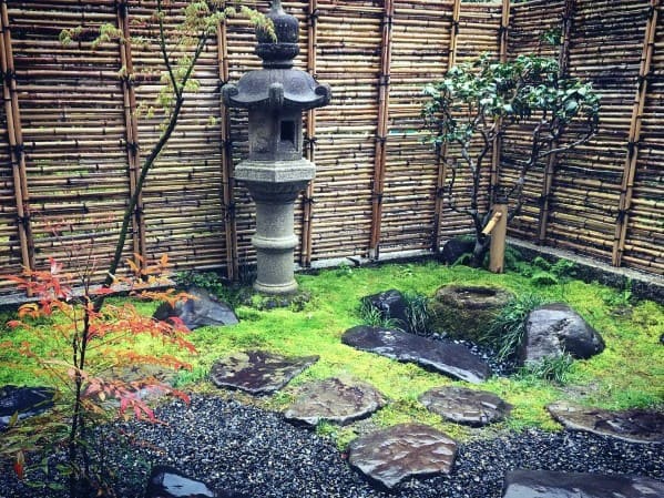 Rustic bamboo fence surrounding a traditional Japanese garden with stone lantern, moss, and stepping stones.