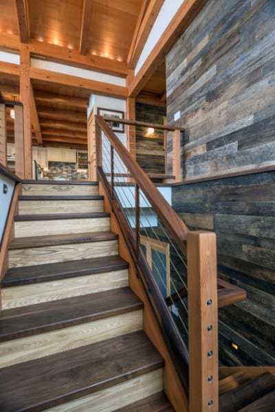 Wooden staircase with cable railing and rustic wood-paneled wall in a modern interior.