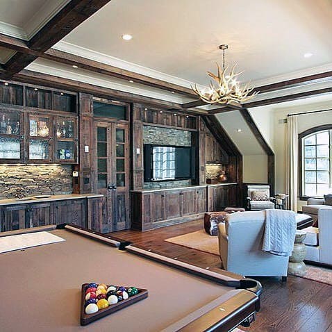 Rustic billiard room with stone accents, antler chandelier, and built-in wooden cabinetry.