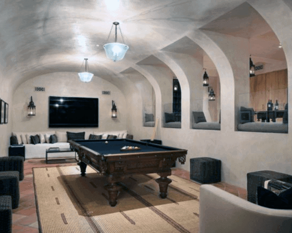 Billiard room with arched walls wood pool table cozy seating and mounted flat screen TV.