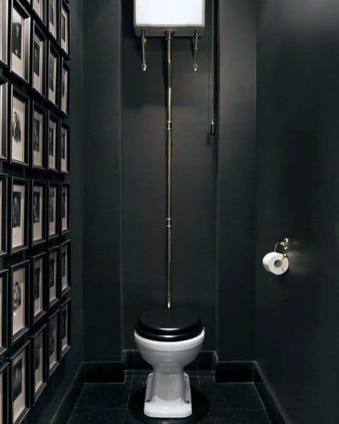 Vintage black bathroom with high-tank toilet and wall gallery of framed black-and-white photos.