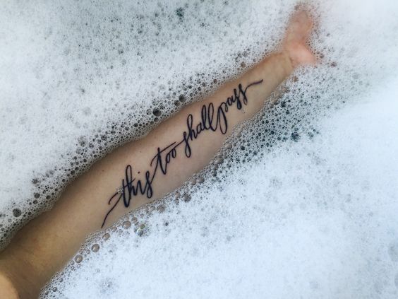 A beautiful "This too shall pass" tattoo in elegant script, emphasizing strength and impermanence, captured in a soothing bubble bath setting.