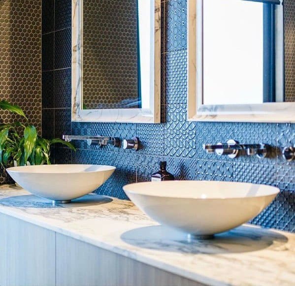 Textured blue accent wall with dual white vessel sinks and marble countertop.