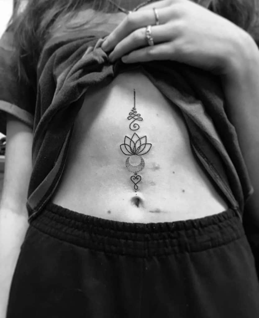 Unalome tattoo with a lotus and crescent moon on the abdomen, symbolizing spiritual enlightenment, balance, and personal growth.