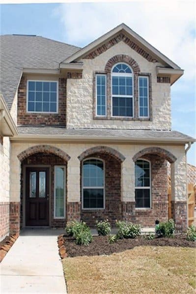 Two-story home with a combination of brick and stone cladding, arched windows and porch, and a welcoming entryway with landscaped accents