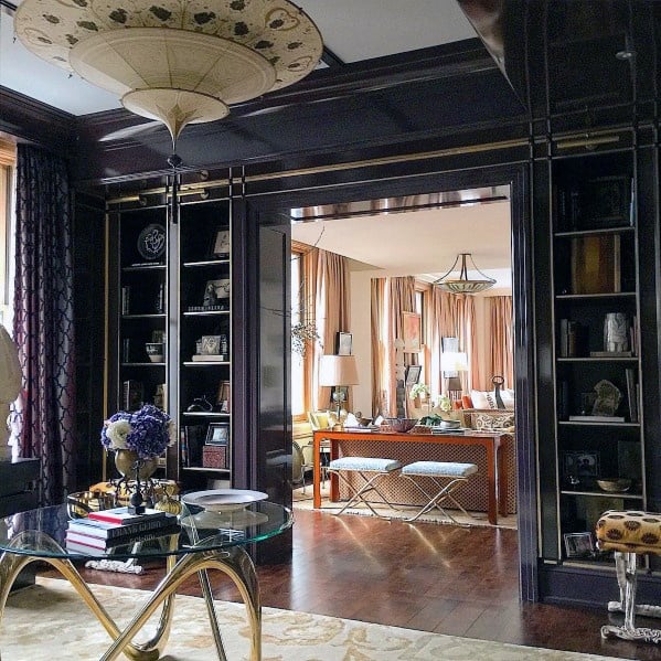 Elegant dark wood built-in bookcases framing a doorway, adorned with books, sculptures, and picture frames, seamlessly connecting luxurious living spaces with warm, rich tones