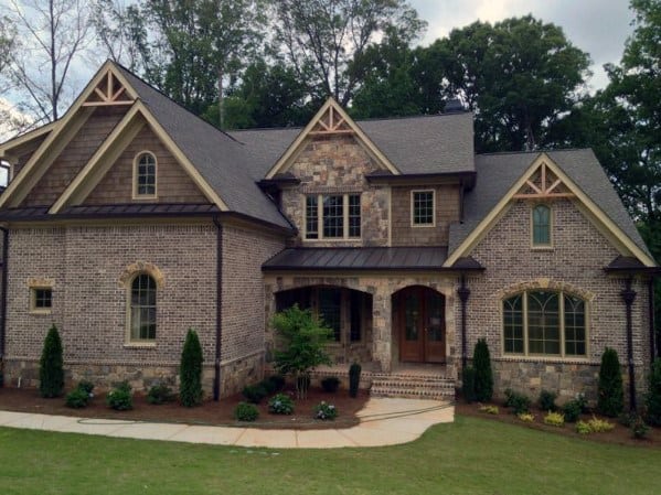 Charming home with brick and stone cladding, gabled rooflines, decorative trim, and a covered porch surrounded by lush greenery