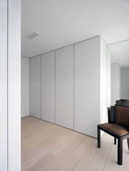 Minimalist room with large white closet, light wood flooring, and a dark wooden chair in the corner