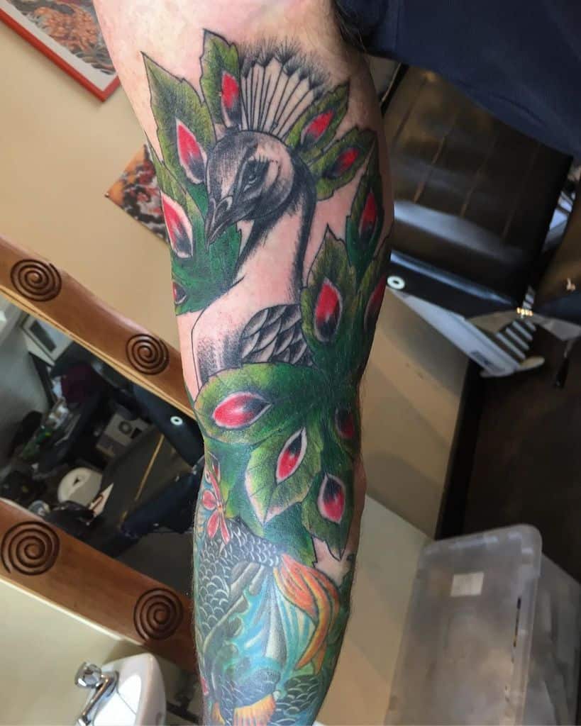 Vibrant peacock tattoo with rich green feathers and red eye patterns, covering the forearm with intricate details.
