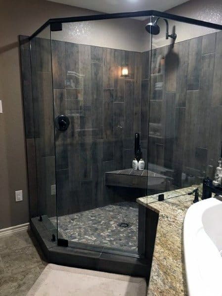 Modern bathroom with a glass-enclosed shower, dark tile walls, a corner bench, and pebble stone floor tiles