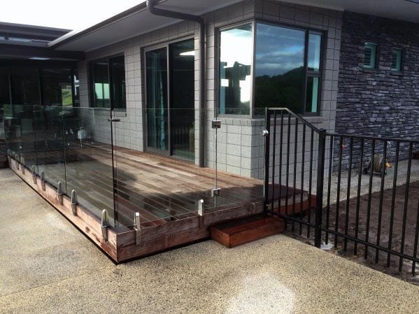 Modern patio with glass railing and wooden deck attached to a contemporary house