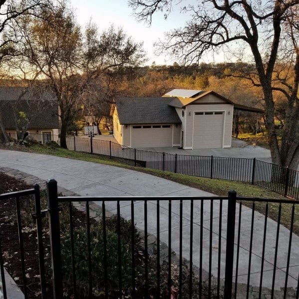 A house with a long driveway, encircled by trees and a sturdy fence in a rural setting at sunset