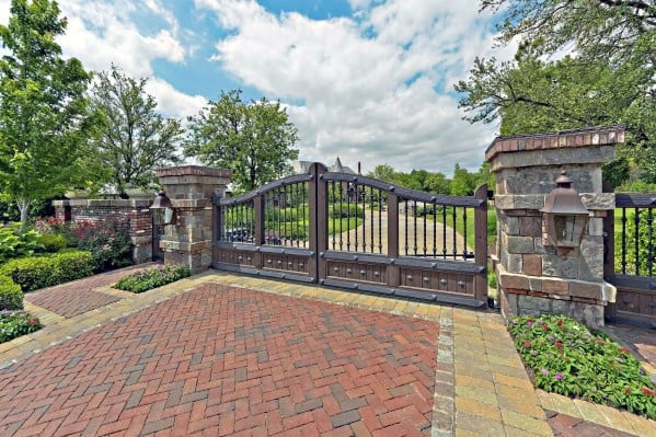 Elegant driveway gate with wrought iron detailing and wood panels flanked by stone pillars.