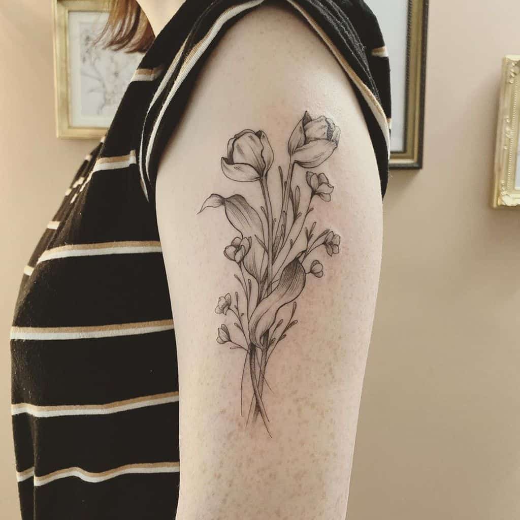 A finely detailed tulip tattoo on the upper arm, featuring multiple flowers with intricate shading, delicate leaves, and small floral accents.