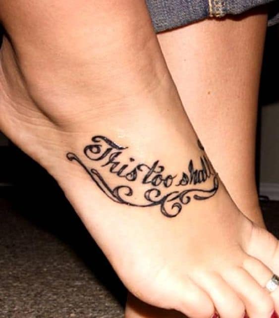 A "This Too Shall Pass" tattoo in cursive on the top of a person's foot.