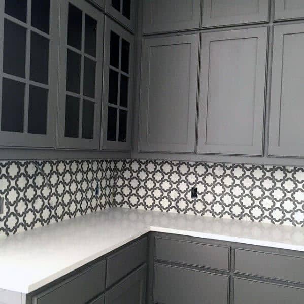 Grey kitchen with paneled cabinets, white countertops, and a patterned tile backsplash for a bold contrast.