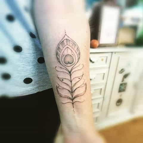 Minimalist peacock feather tattoo on the forearm, featuring fine linework, geometric elements, and delicate dot detailing.