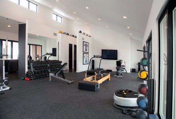 Bright home gym with rubber flooring, weight rack, cardio equipment, and a wall-mounted TV.