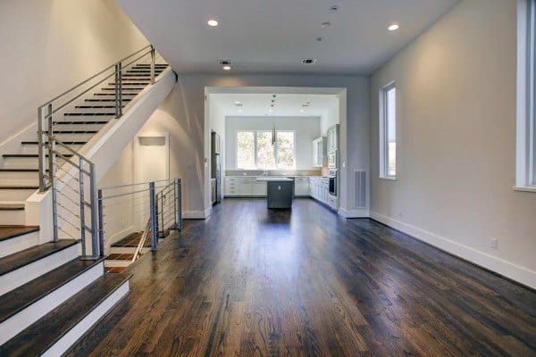 Spacious modern living room with wooden flooring, a prominent staircase, and an open kitchen at the far end