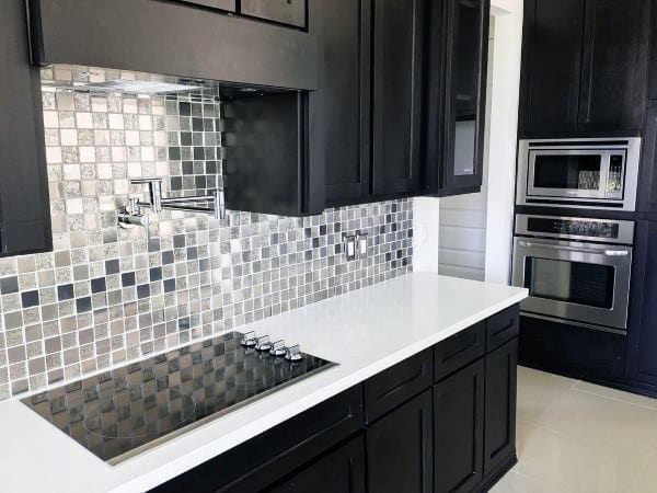 Modern kitchen with black cabinets, mirrored mosaic tile backsplash, and white countertop.
