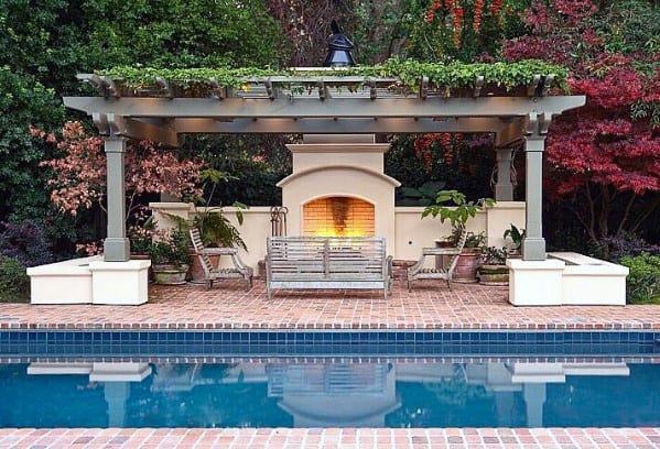 Brick pergola with fireplace, patio, and pool, embraced by lush greenery
