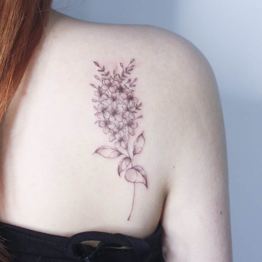 Delicate fine-line lilac flower tattoo on the upper back, featuring soft shading and an elegant, minimalist botanical design.