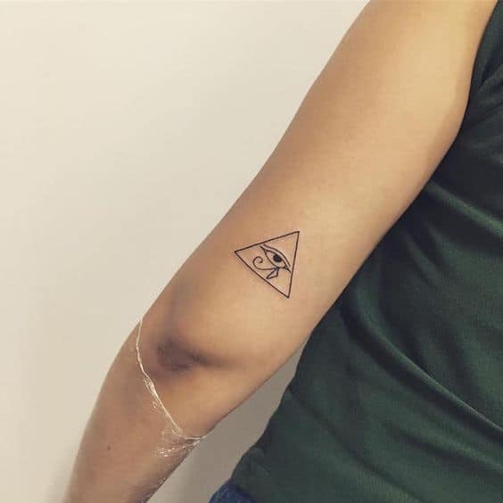 Minimalist tattoo of the Eye of Horus inside a small triangle, inked in fine black lines on the back of the arm.