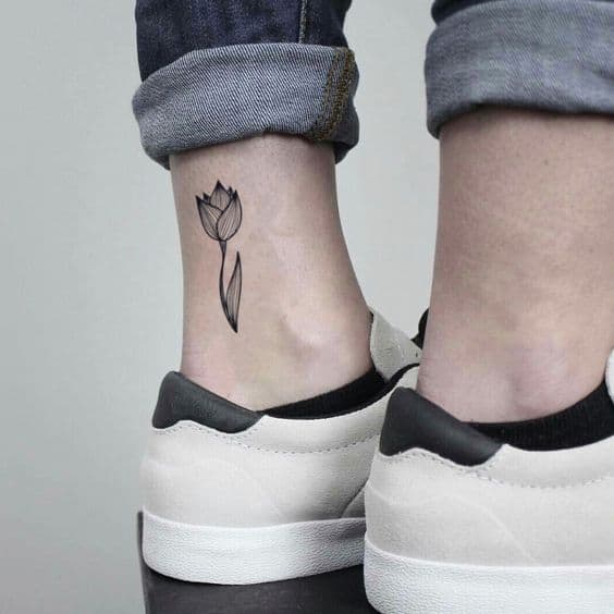 A minimalist black-line tulip tattoo on the ankle, featuring a delicate flower with a thin stem and simple leaf design.