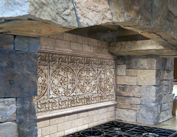 Rustic kitchen with a detailed decorative tile inlay, natural stone surround, and a robust range hood design