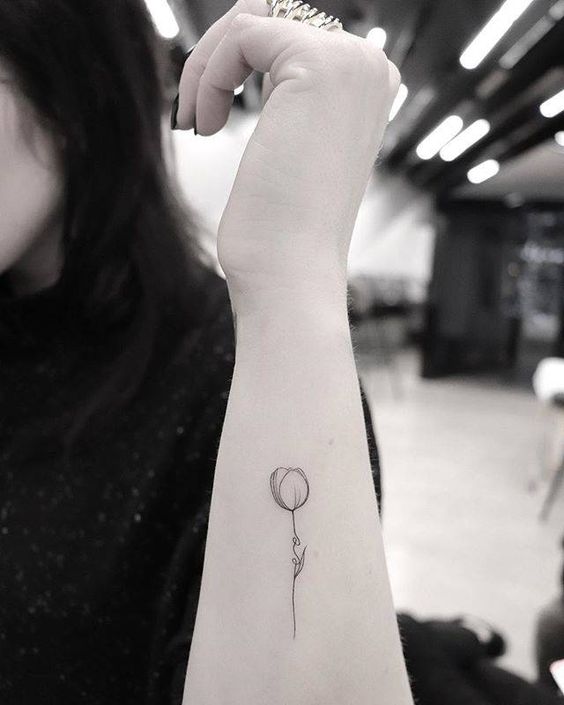 A minimalist black-line tulip tattoo on the forearm, featuring a delicate stem and soft, rounded flower with a slender design.