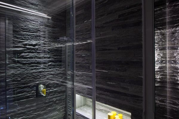 Modern shower featuring dark slate tiles, glass doors, and yellow shampoo bottles on a sleek built-in shelf