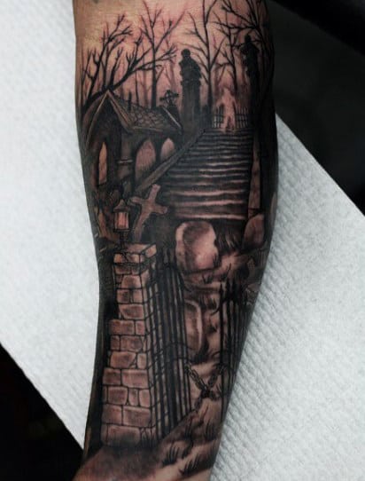 A tattoo featuring a gothic graveyard with a stone gate and staircase leading to a crypt