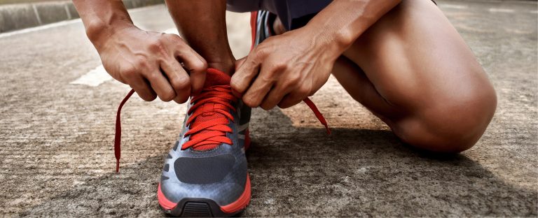 Muscular man ties laces of grey and orange running shoes.