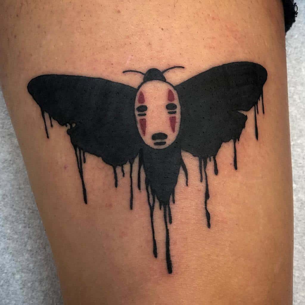 Black ink tattoo of a moth with No-Face’s mask from Spirited Away as its body, featuring dripping, melting wing details