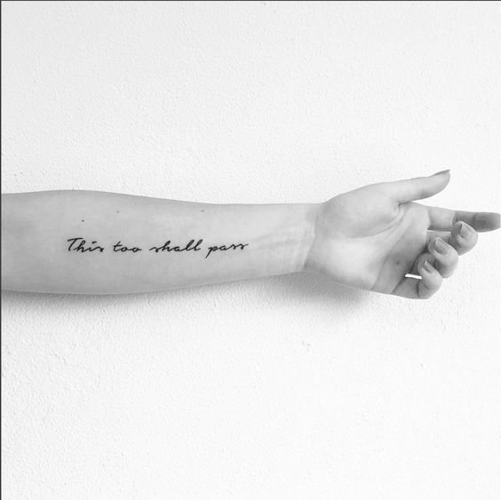 "This too shall pass" tattoo in cursive on the forearm.