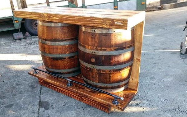Wooden bar with two barrels supporting a rustic countertop on an outdoor surface