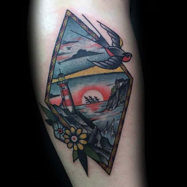 Tattoo of a lighthouse, swallow, and sunset in a diamond frame with flowers at the base
