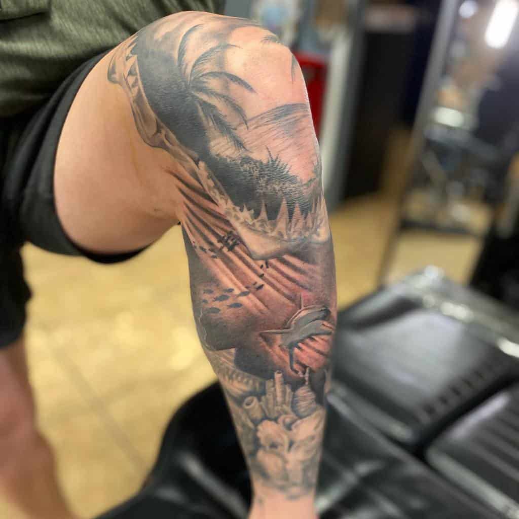 Detailed leg sleeve tattoo, featuring a dramatic scene with a shark, palm trees, and a skull, with intricate design elements