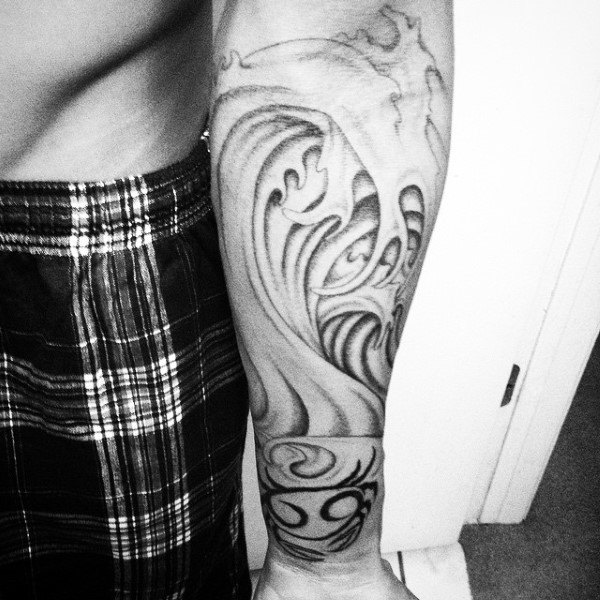 Close-up of a forearm tattoo featuring waves and abstract designs in black ink