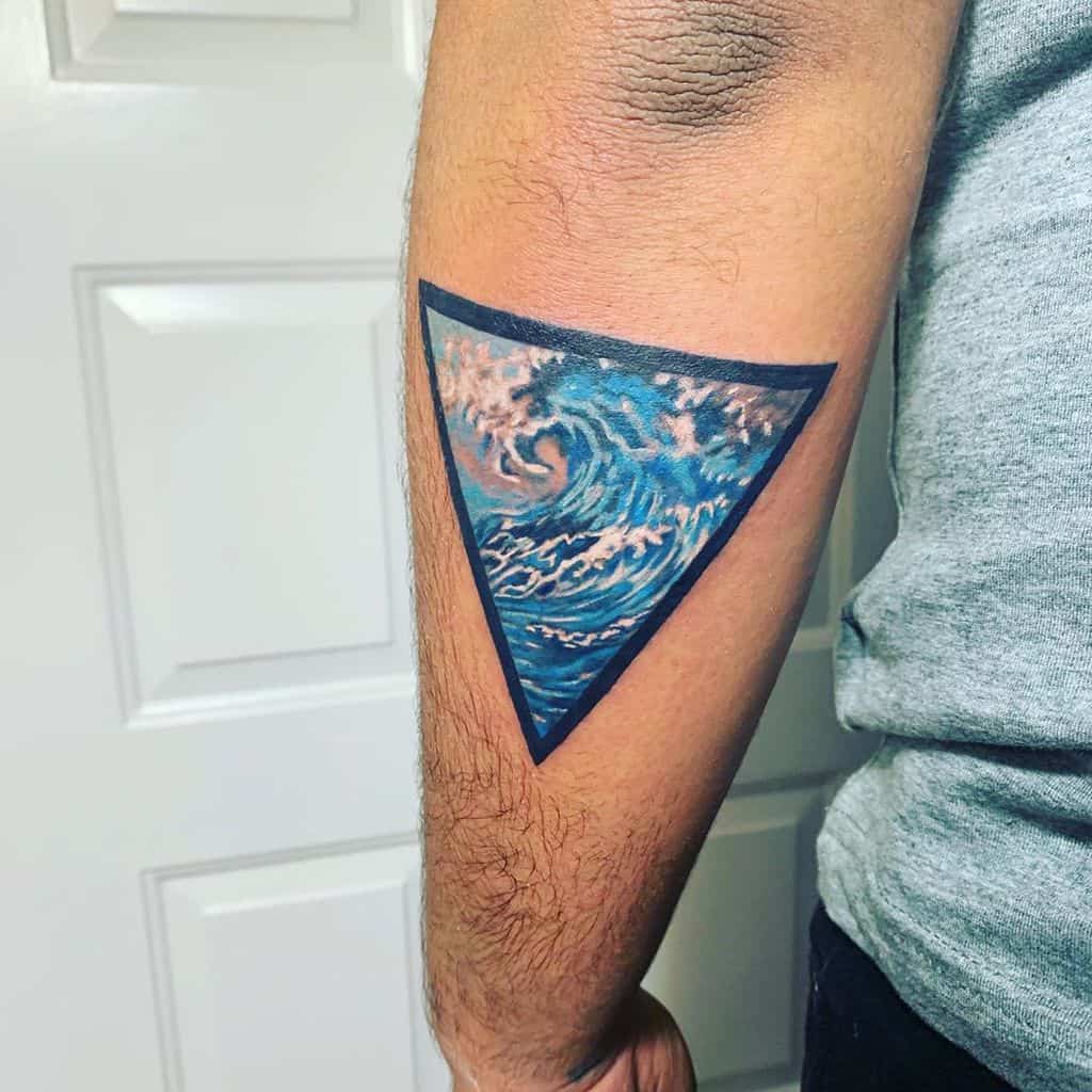 Vibrant tattoo of a crashing ocean wave enclosed within an inverted triangle, featuring rich blue tones and pink highlights