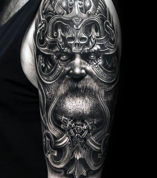 Intricate black and grey tattoo of a Viking warrior face with ornate helmet and beard, symbolizing wisdom, power, and Norse heritage.