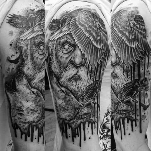 Dark surrealist upper arm tattoo of Odin with ravens and a wolf, featuring bold shading, dripping ink effects, and intense expression.