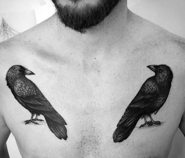 Minimalist black and grey chest tattoos of Huginn and Muninn facing each other, perched symmetrically above the pectorals.
