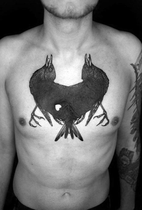 Bold black chest tattoo of Huginn and Muninn mirrored in flight with beaks open, forming a heart-like silhouette in the center.