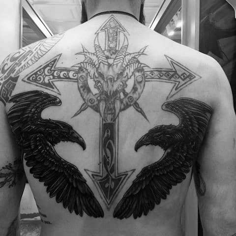 Large back tattoo featuring black raven wings beneath a detailed goat skull, set over a bold Nordic-style cross with intricate patterns.