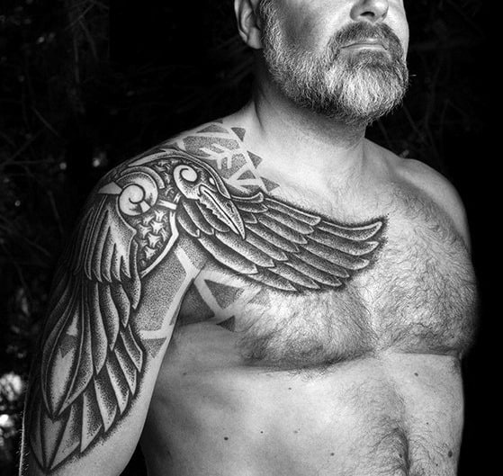 Dotwork tattoo of a stylized raven with extended wing spanning from shoulder to chest, featuring Norse geometric patterns and bold shading.