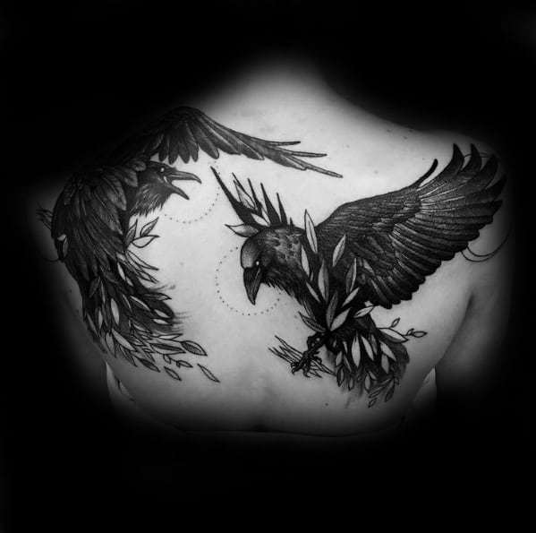Back tattoo of Huginn and Muninn in flight with leafy branches and dotted circles, combining natural elements with Norse symbolism in black ink.
