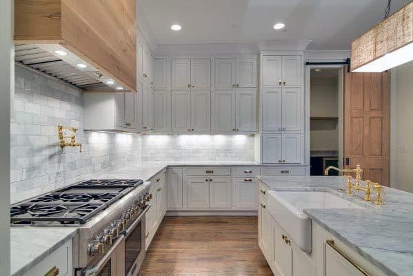 White kitchen with gold fixtures, marble countertops, and subway tile backsplash.
